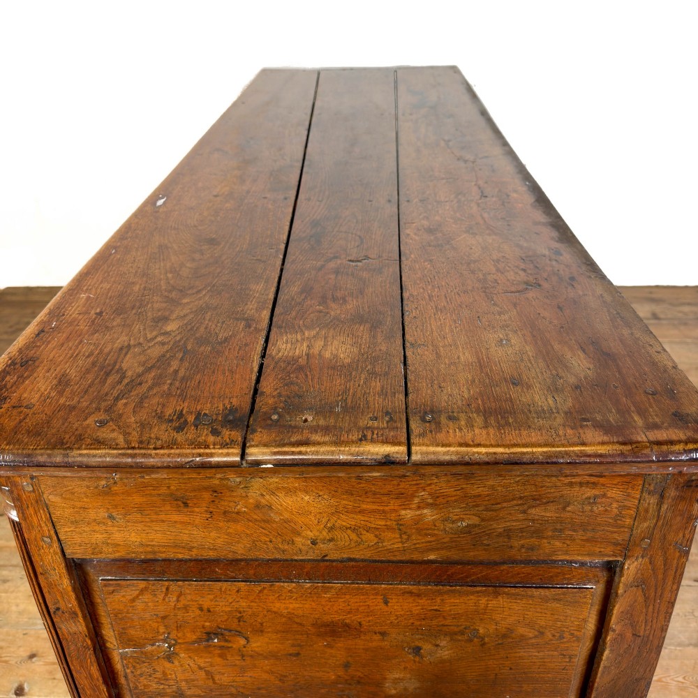 An antique Georgian oak dresser base with multiple drawers, fielded panel cupboard doors, and brass swan-neck handles on a bracket feet base. View VIII