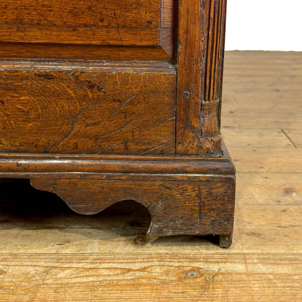 An antique Georgian oak dresser base with multiple drawers, fielded panel cupboard doors, and brass swan-neck handles on a bracket feet base. View XIII