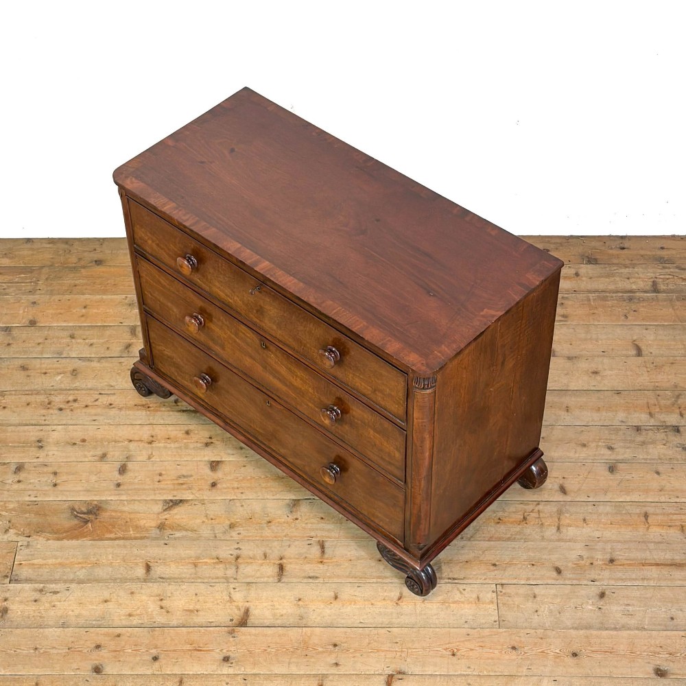 A William IV dark mahogany chest of drawers featuring three long drawers with turned knobs, brass escutcheons, and carved scroll feet. View III