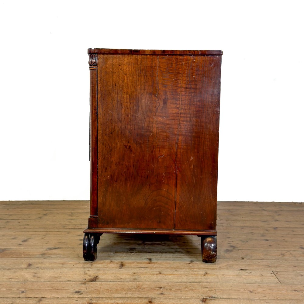 A William IV dark mahogany chest of drawers featuring three long drawers with turned knobs, brass escutcheons, and carved scroll feet. View IV