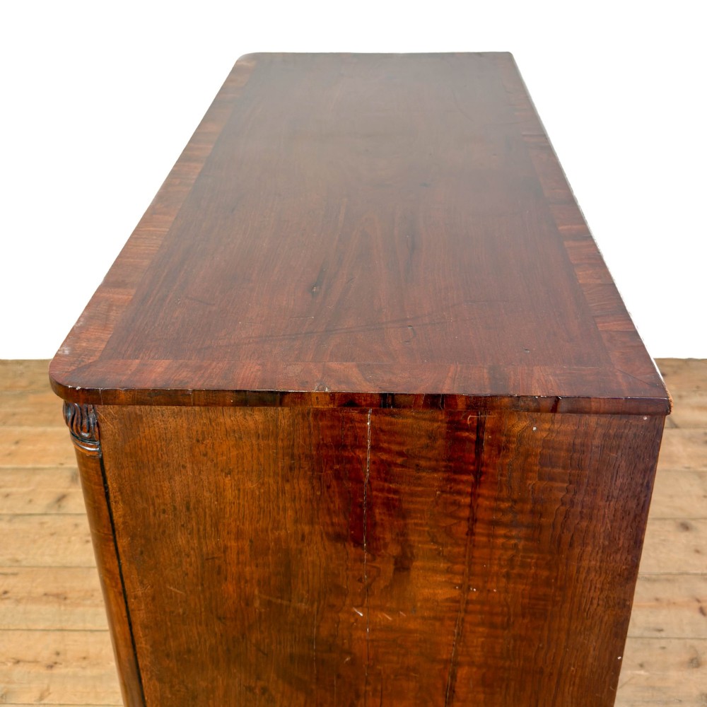 A William IV dark mahogany chest of drawers featuring three long drawers with turned knobs, brass escutcheons, and carved scroll feet. View V