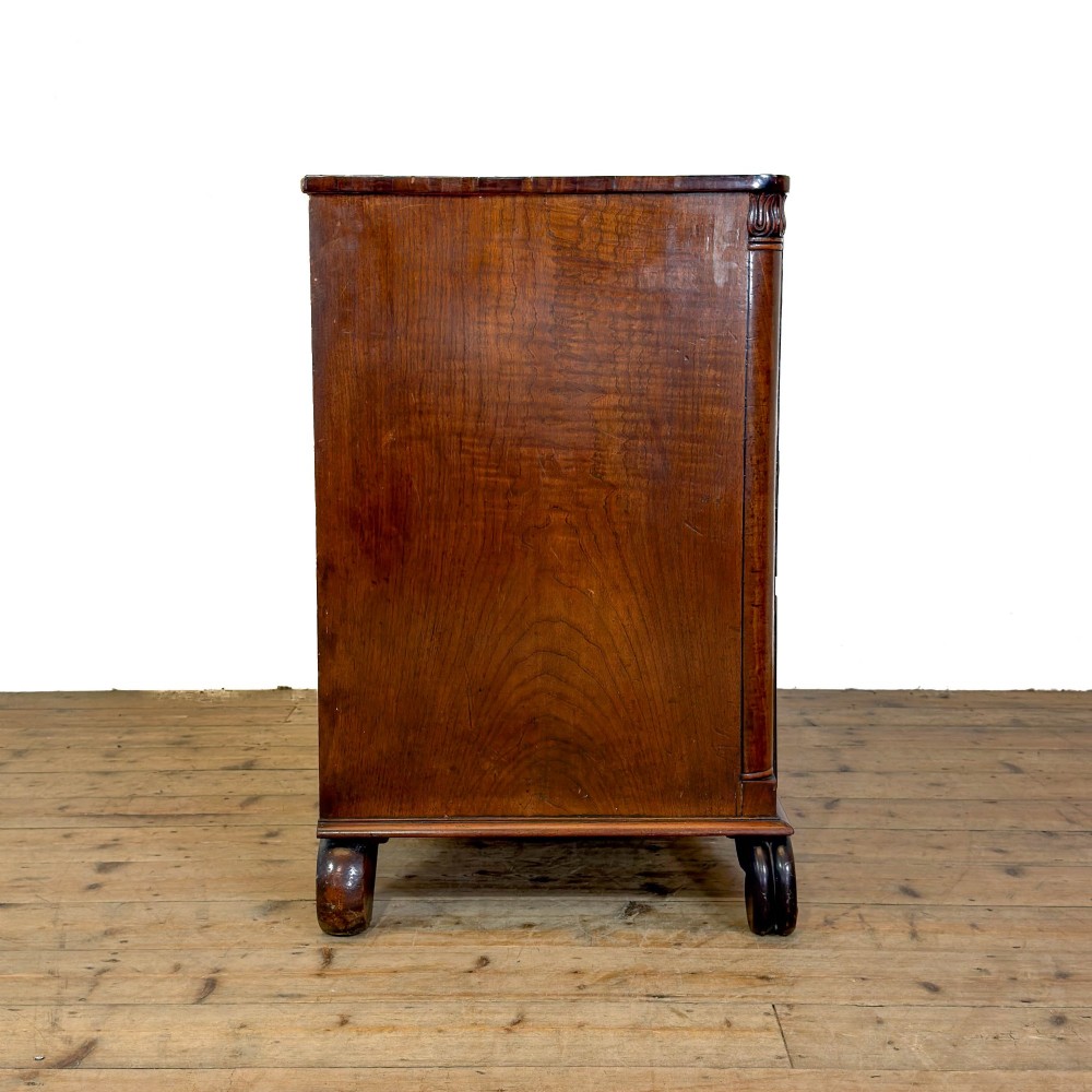 A William IV dark mahogany chest of drawers featuring three long drawers with turned knobs, brass escutcheons, and carved scroll feet. View VIII