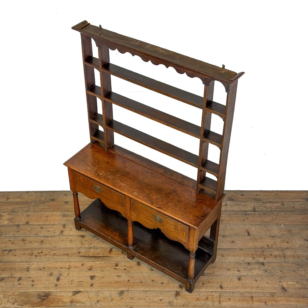 An antique oak Welsh dresser featuring an open tiered plate rack with a scalloped top frieze over two drawers and a bottom pot board shelf. View IV