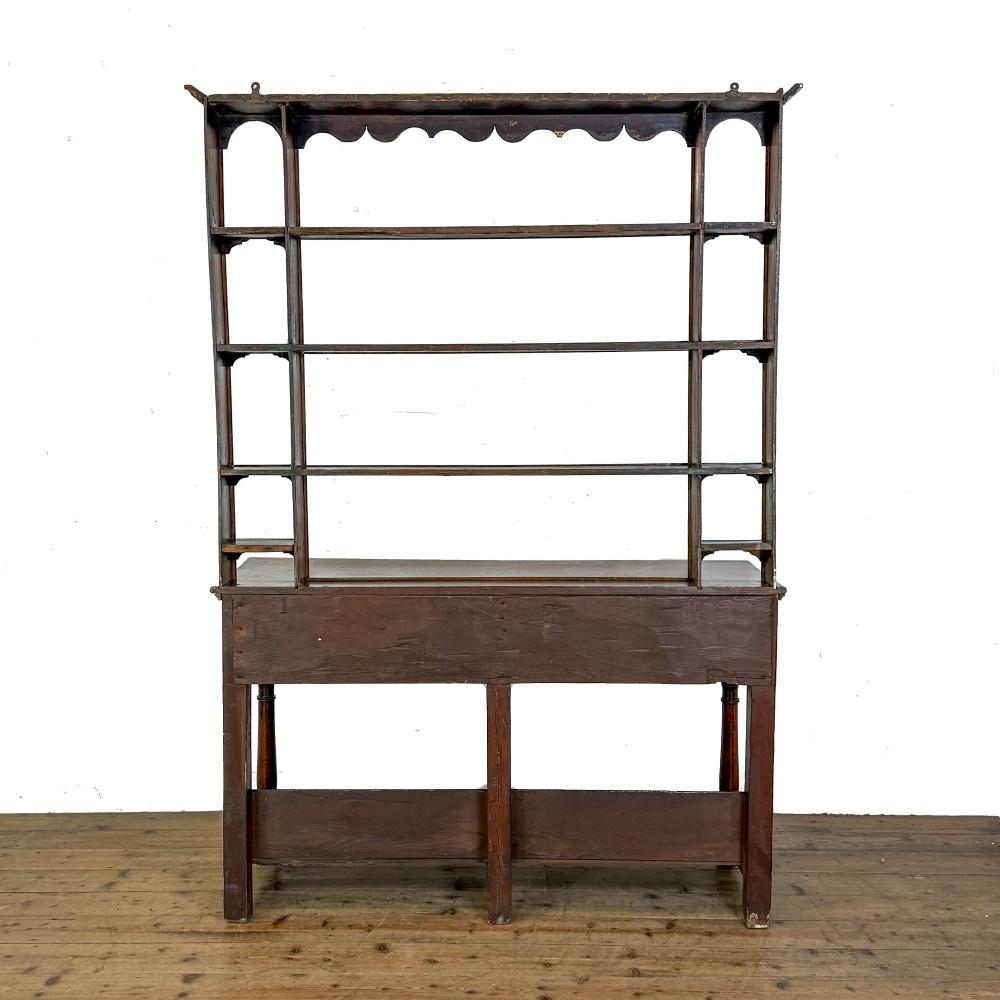 An antique oak Welsh dresser featuring an open tiered plate rack with a scalloped top frieze over two drawers and a bottom pot board shelf. View VII