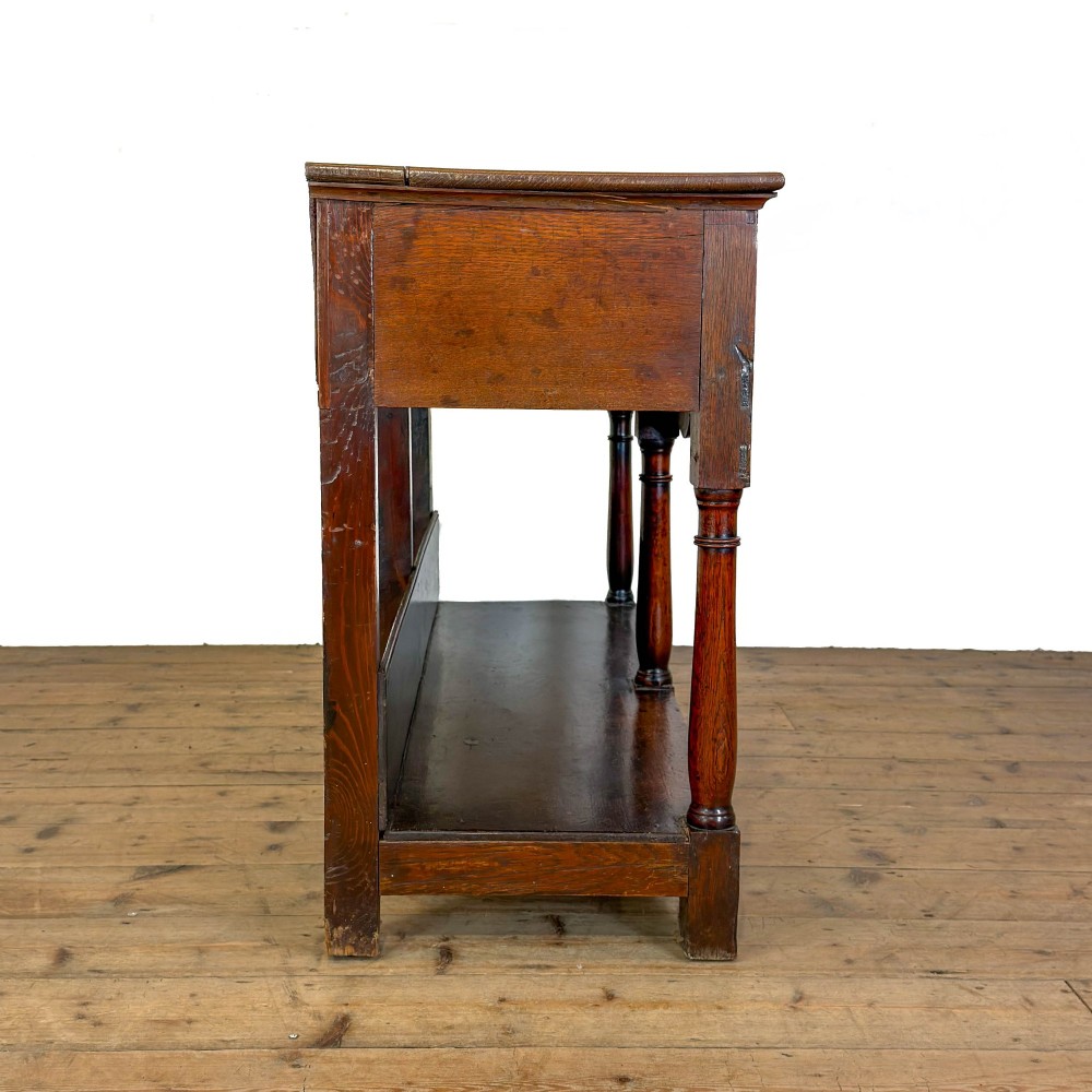An antique oak dresser base featuring two drawers with brass backplate handles, shaped lower aprons, turned front legs, and an open potboard shelf. View II