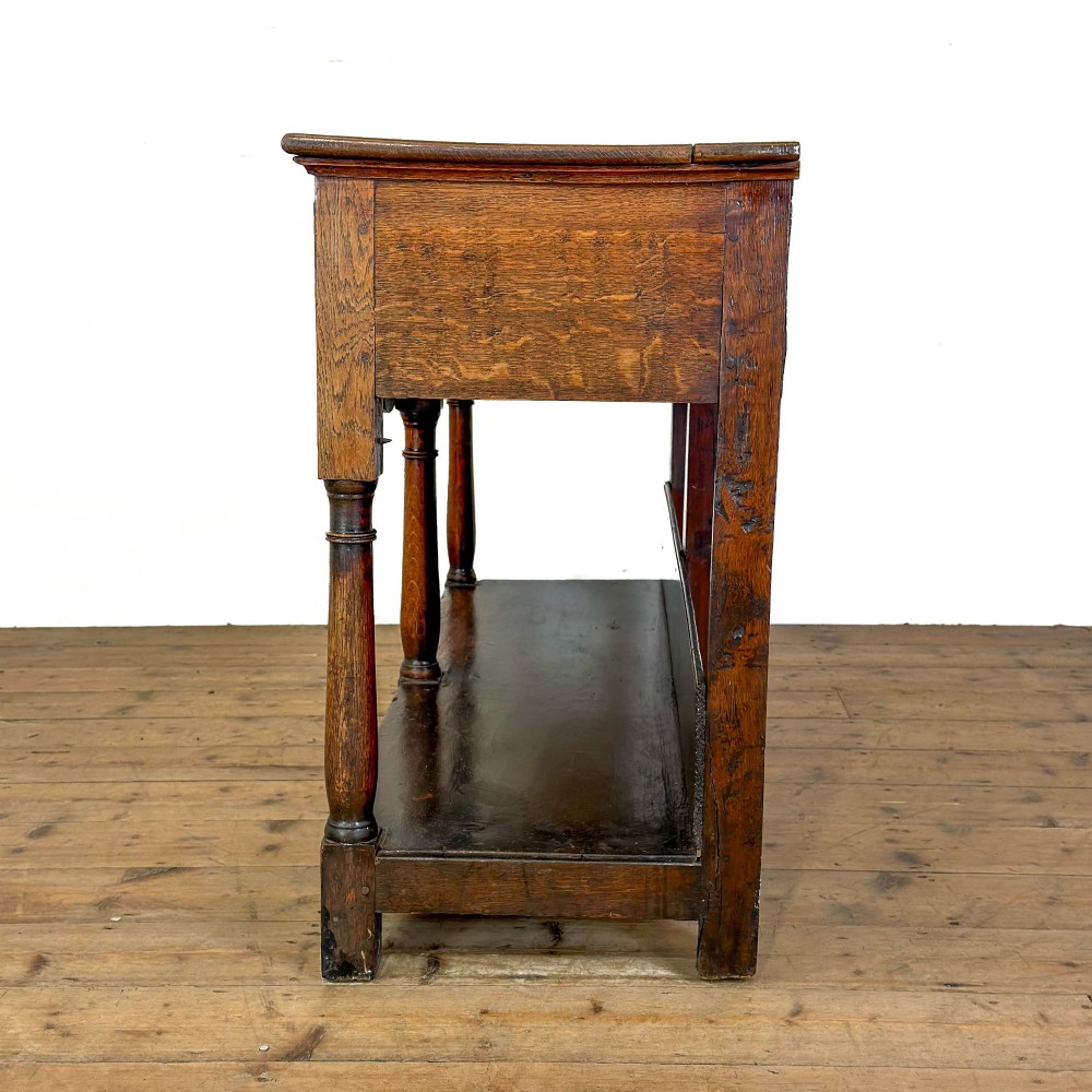 An antique oak dresser base featuring two drawers with brass backplate handles, shaped lower aprons, turned front legs, and an open potboard shelf. View V