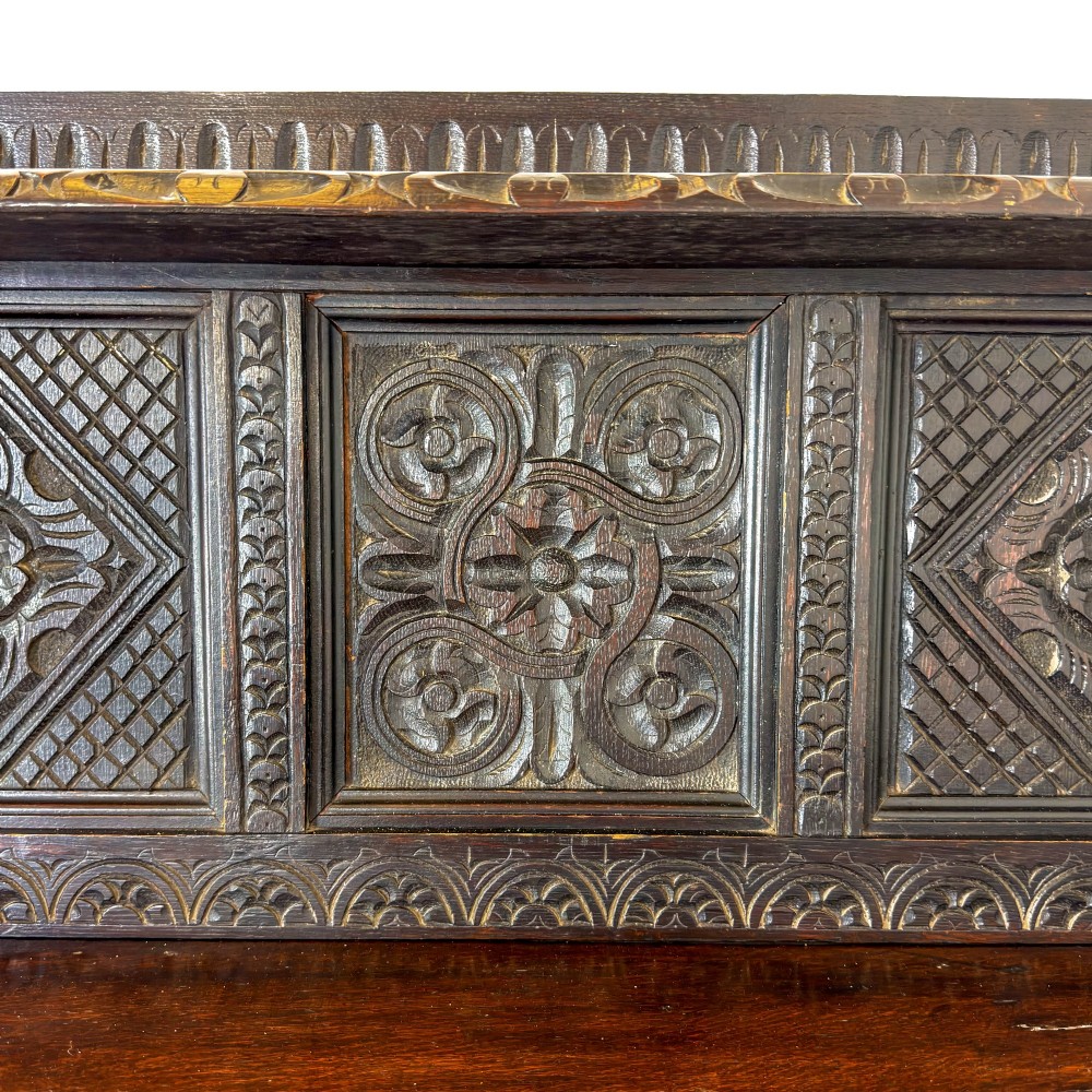 A dark carved oak Victorian sideboard with a tiered top shelf, detailed geometric carved door panels, brass hinges, and turned legs with a lower stretcher rail. View IV