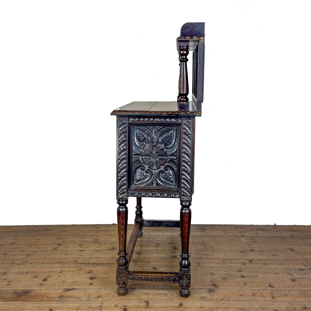 A dark carved oak Victorian sideboard with a tiered top shelf, detailed geometric carved door panels, brass hinges, and turned legs with a lower stretcher rail. View IX