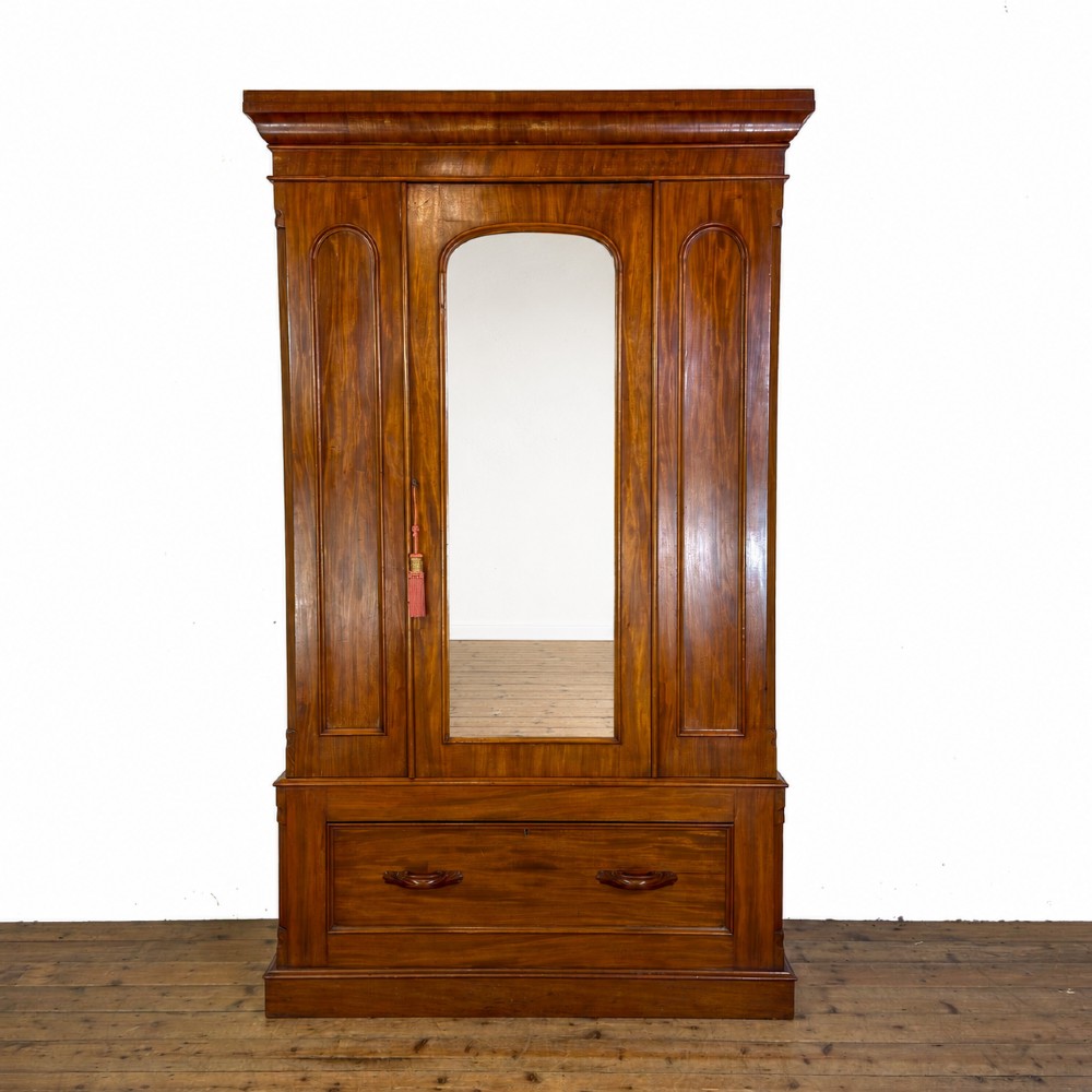 A tall Victorian mahogany wardrobe featuring an arched central mirrored door flanked by wooden side panels over a wide base drawer. View II