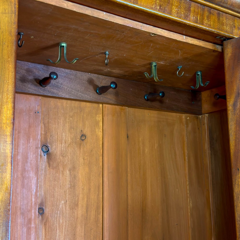 A tall Victorian mahogany wardrobe featuring an arched central mirrored door flanked by wooden side panels over a wide base drawer. View V