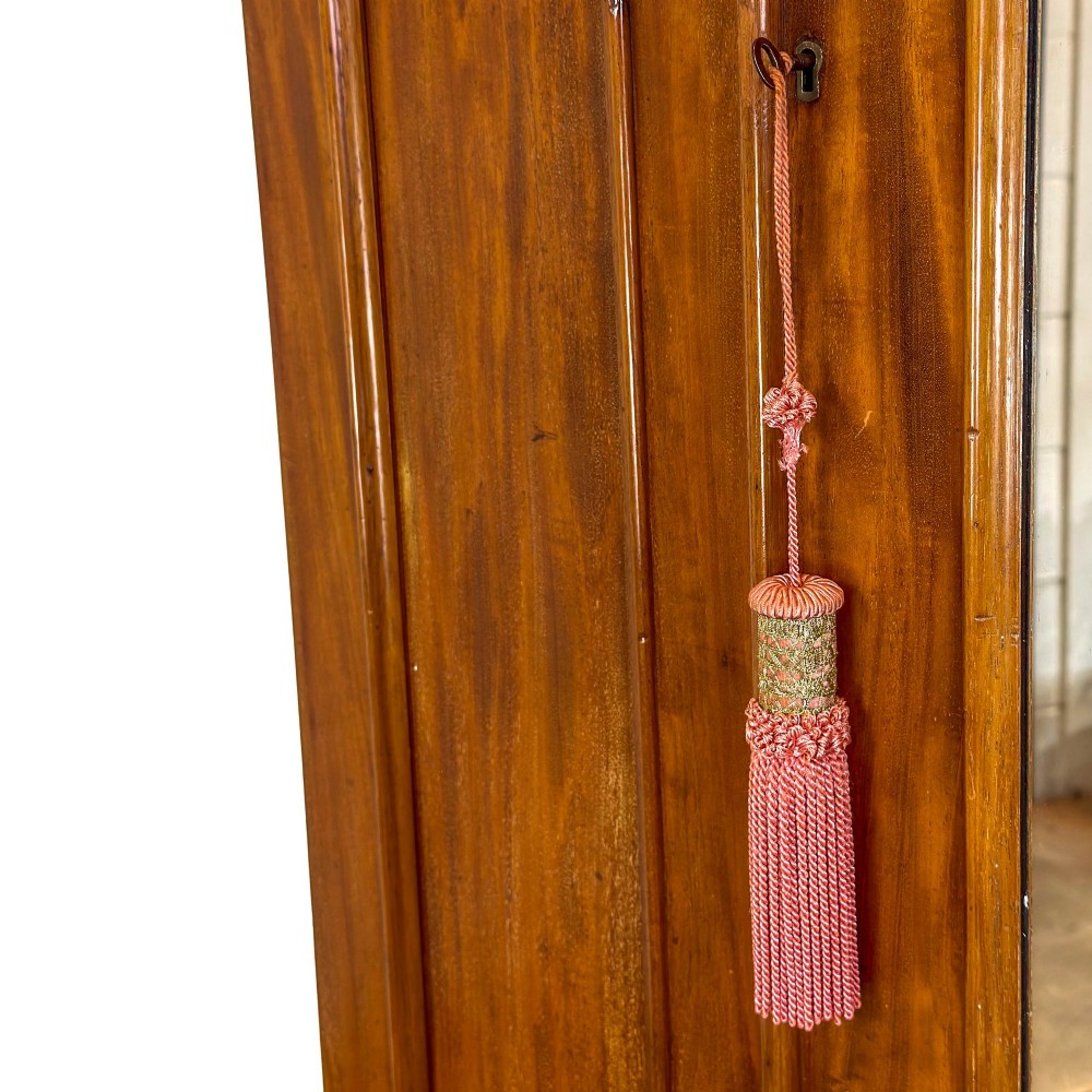 A tall Victorian mahogany wardrobe featuring an arched central mirrored door flanked by wooden side panels over a wide base drawer. View VII
