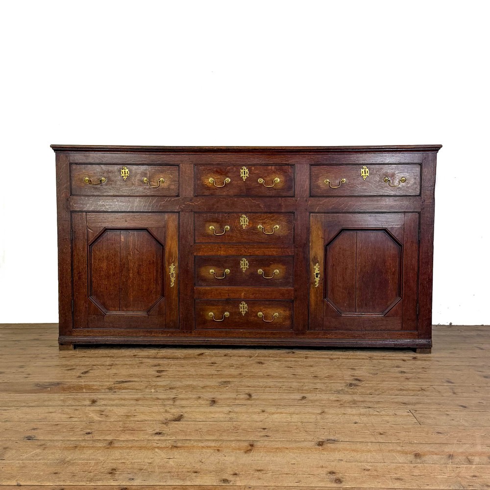 An early nineteenth-century dark oak dresser base featuring multiple drawers with brass handles, twin panelled cupboard doors, and a solid wood plinth base.