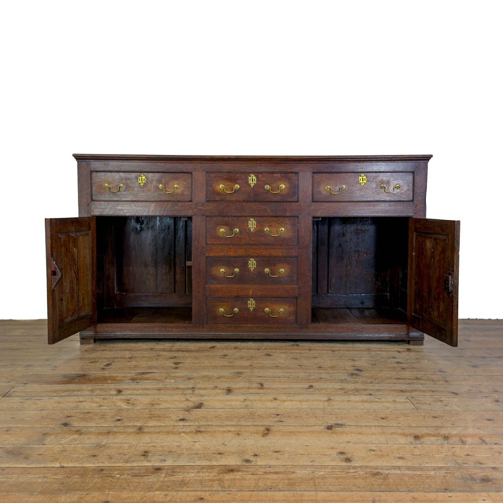 An early nineteenth-century dark oak dresser base featuring multiple drawers with brass handles, twin panelled cupboard doors, and a solid wood plinth base. View II