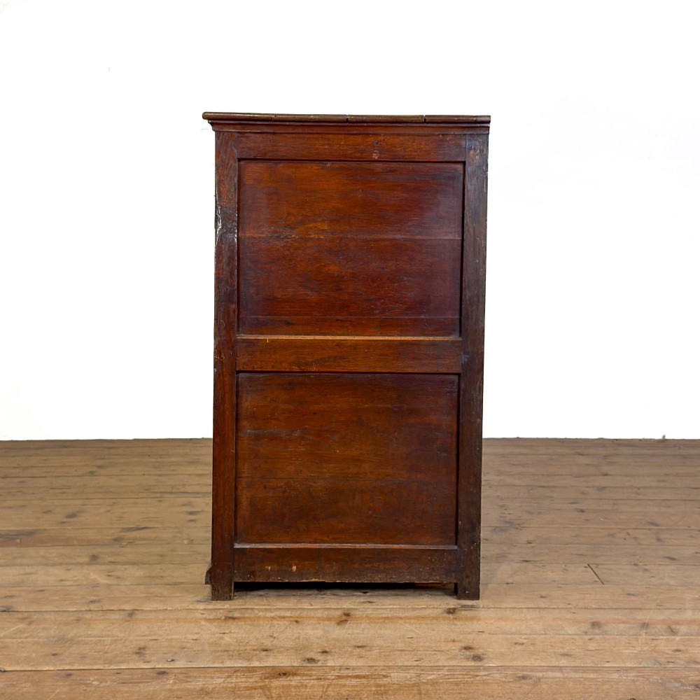An early nineteenth-century dark oak dresser base featuring multiple drawers with brass handles, twin panelled cupboard doors, and a solid wood plinth base. View VI