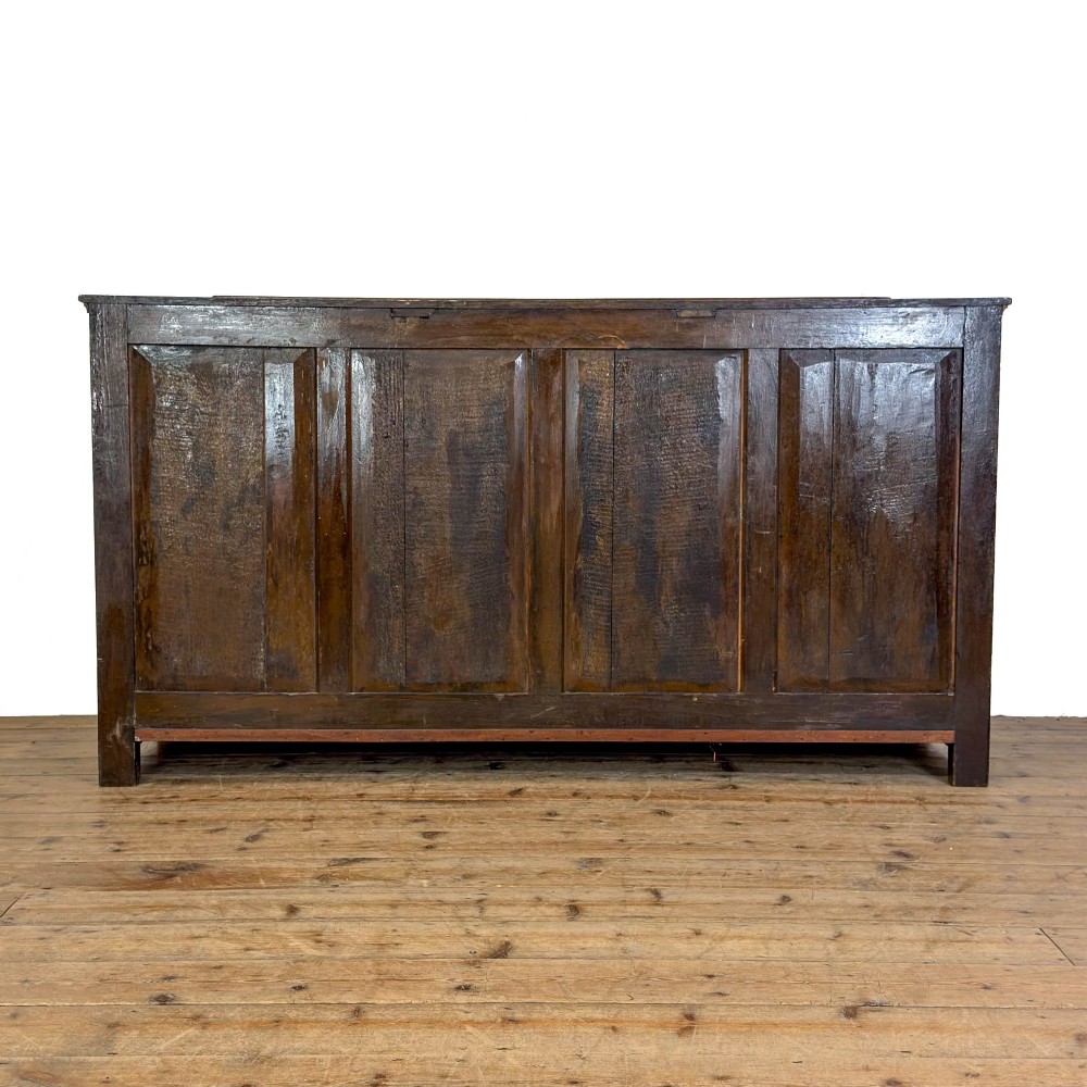 An early nineteenth-century dark oak dresser base featuring multiple drawers with brass handles, twin panelled cupboard doors, and a solid wood plinth base. View VII