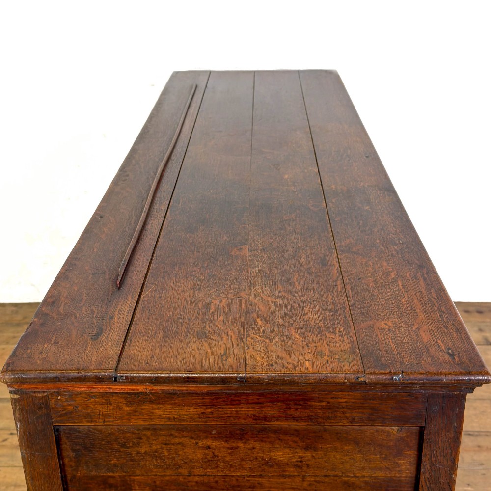 An early nineteenth-century dark oak dresser base featuring multiple drawers with brass handles, twin panelled cupboard doors, and a solid wood plinth base. View IX