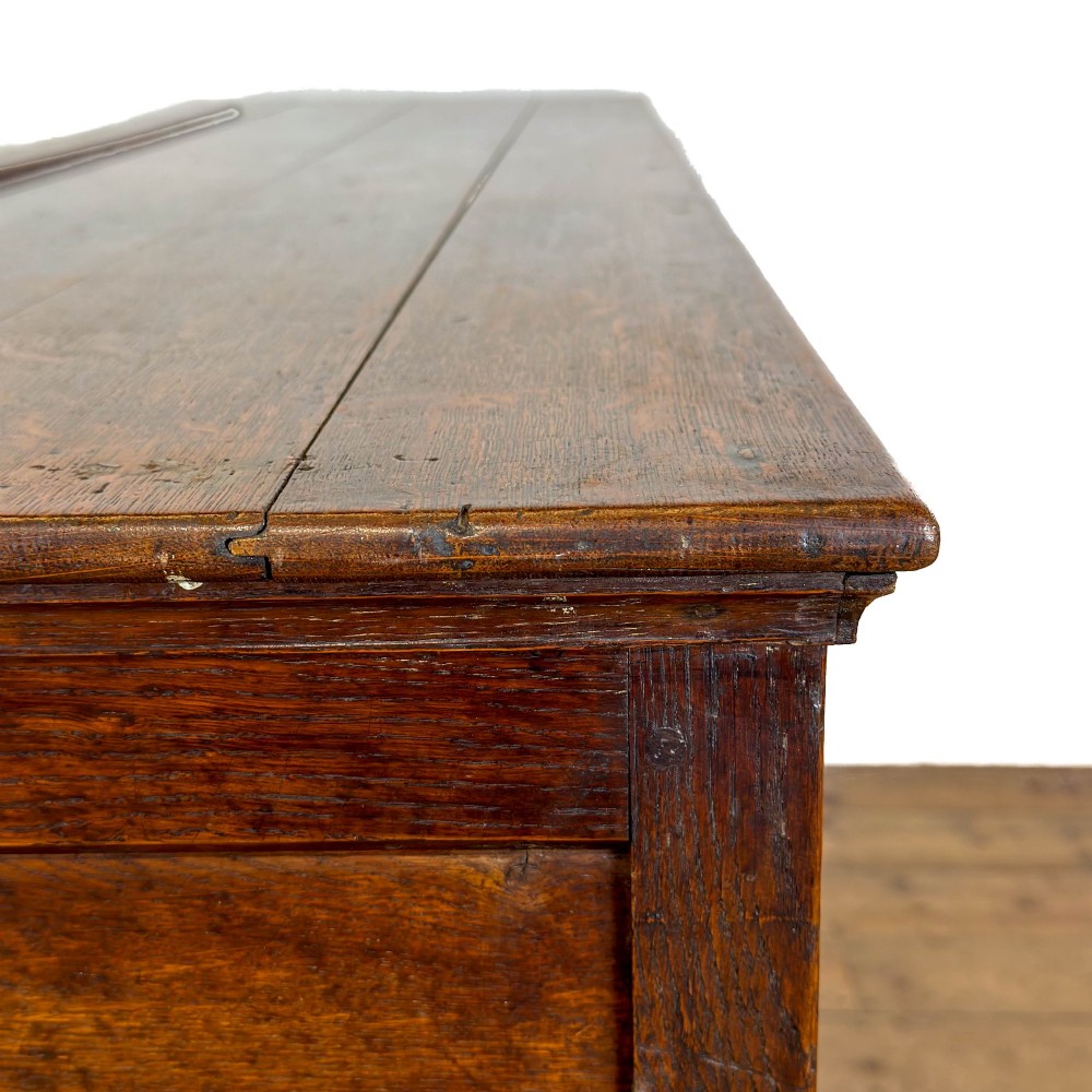 An early nineteenth-century dark oak dresser base featuring multiple drawers with brass handles, twin panelled cupboard doors, and a solid wood plinth base. View X