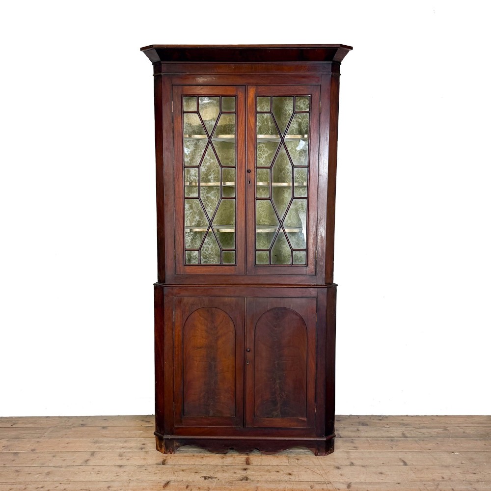 A tall two-part mahogany corner cabinet featuring geometric astragal glazed upper doors above panelled lower doors.