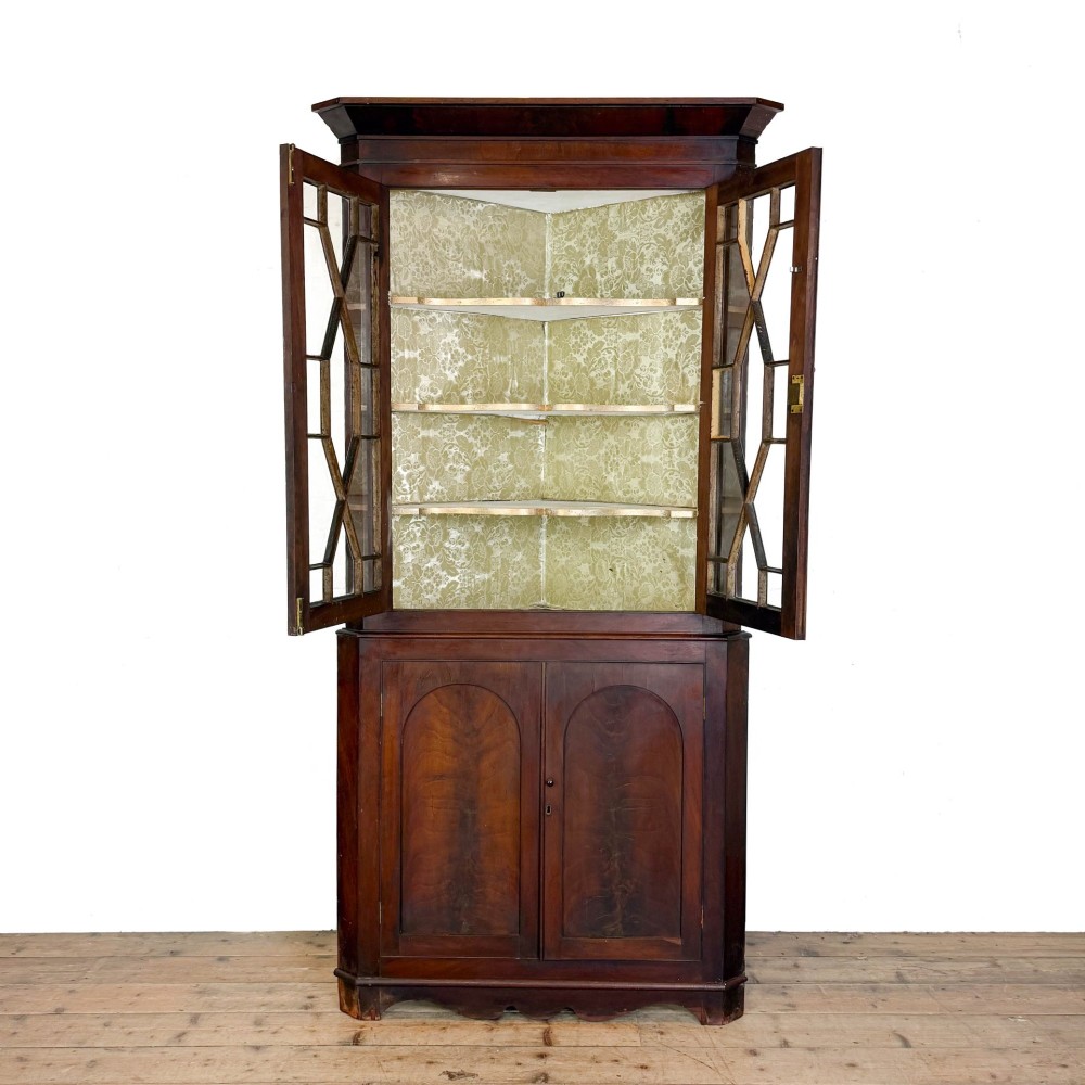 A tall two-part mahogany corner cabinet featuring geometric astragal glazed upper doors above panelled lower doors. View II