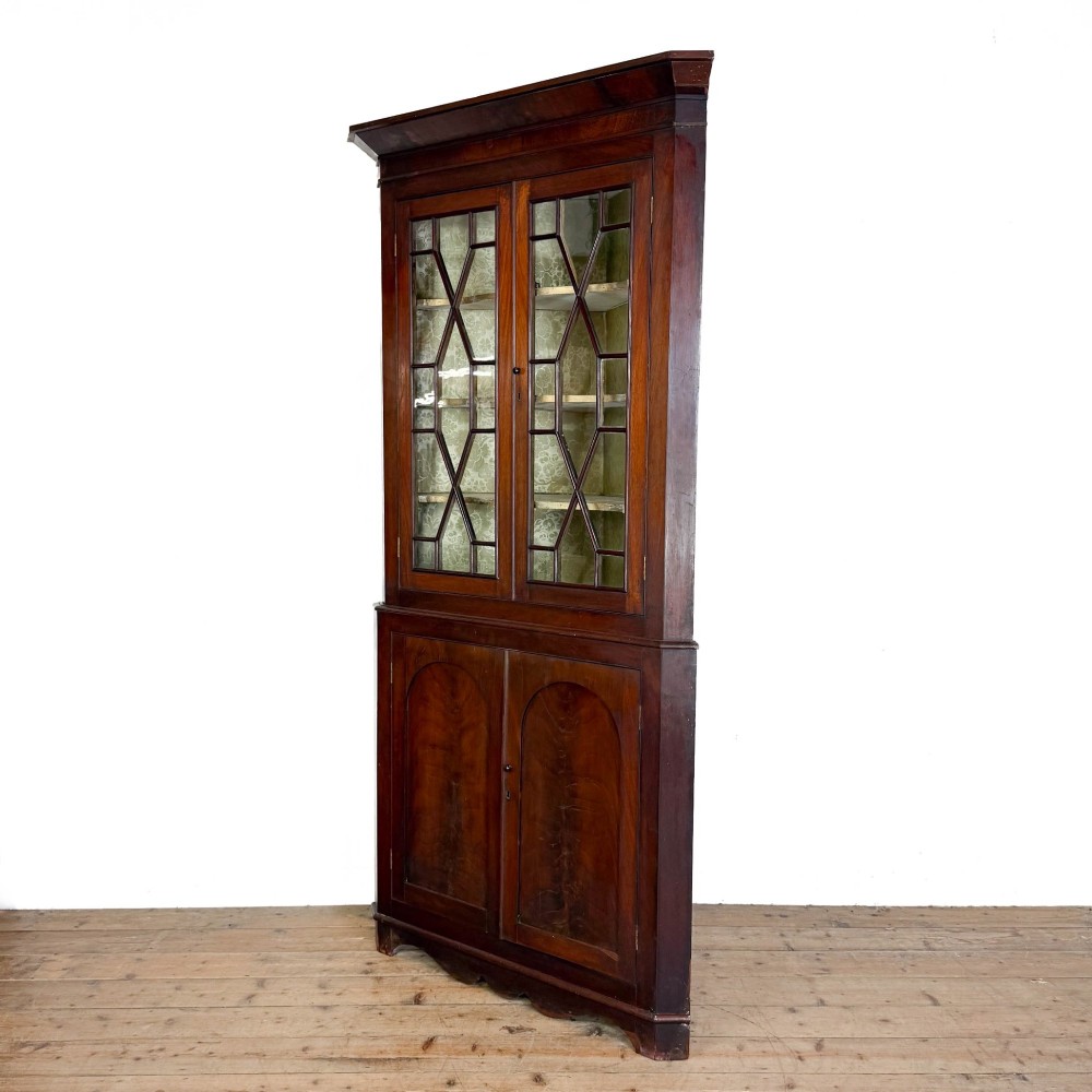 A tall two-part mahogany corner cabinet featuring geometric astragal glazed upper doors above panelled lower doors. View V