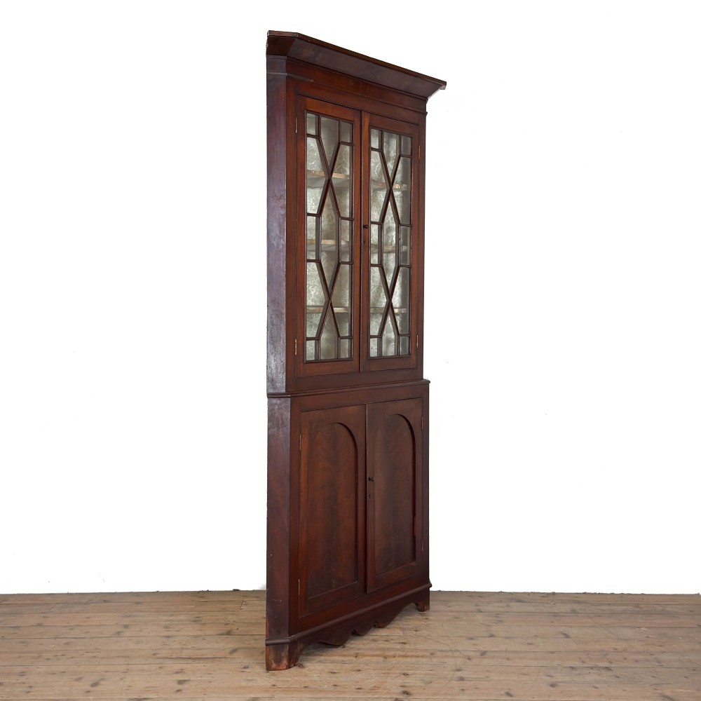 A tall two-part mahogany corner cabinet featuring geometric astragal glazed upper doors above panelled lower doors. View VIII