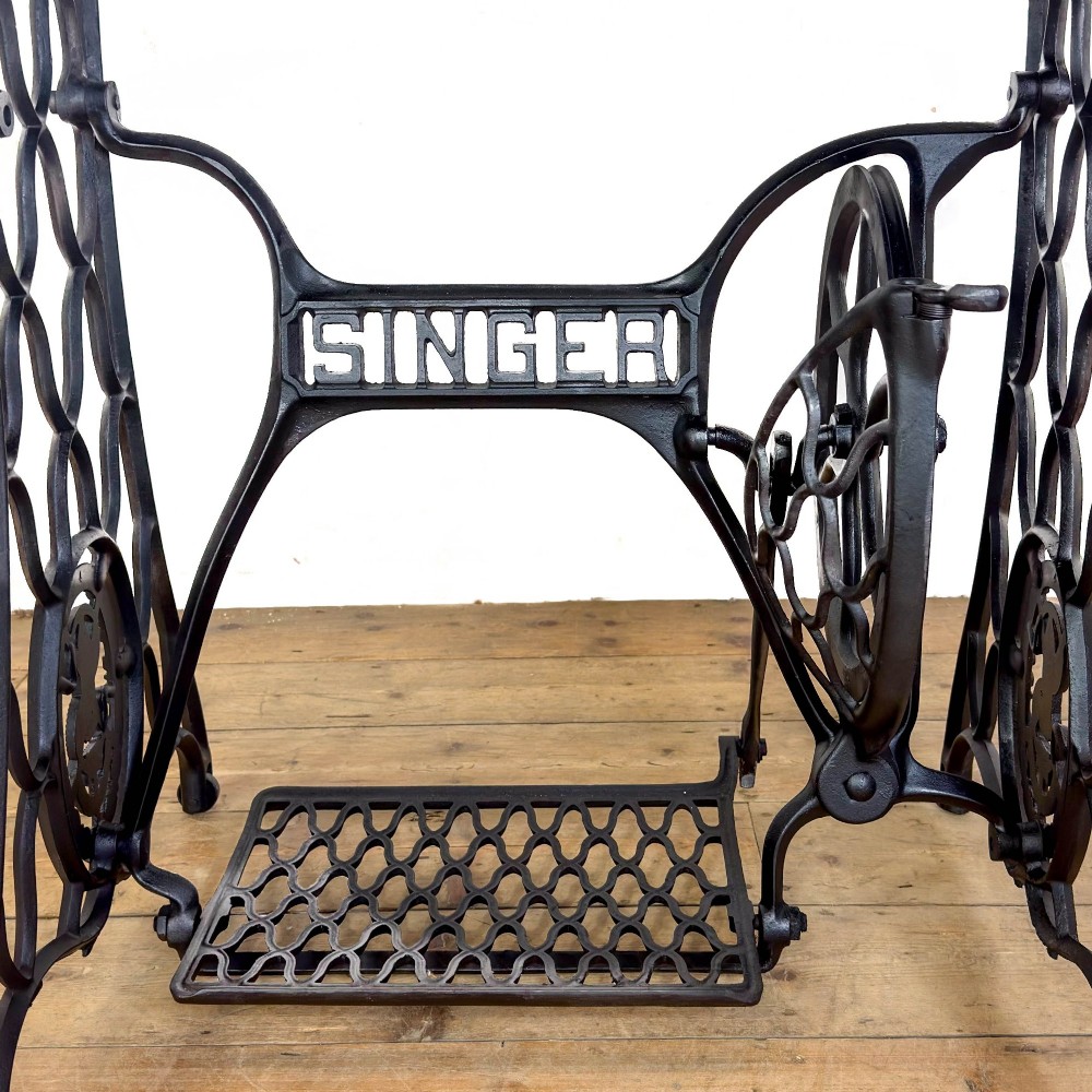An antique black cast iron Singer treadle sewing machine base featuring a central brand crest and flywheel, fitted with a rectangular wooden tabletop. View VI