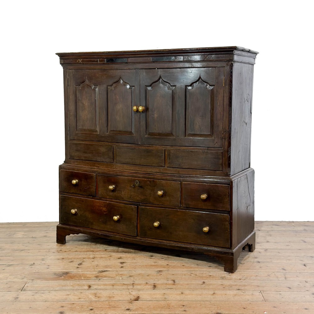 An 18th-century Welsh dark oak Carmarthenshire coffer featuring upper cupboard doors with pointed arch fielded panels above multiple drawers fitted with brass knobs. View II