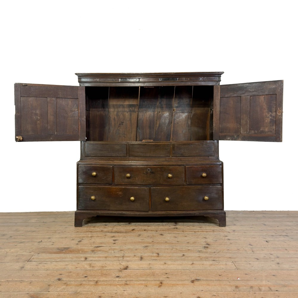 An 18th-century Welsh dark oak Carmarthenshire coffer featuring upper cupboard doors with pointed arch fielded panels above multiple drawers fitted with brass knobs. View VI