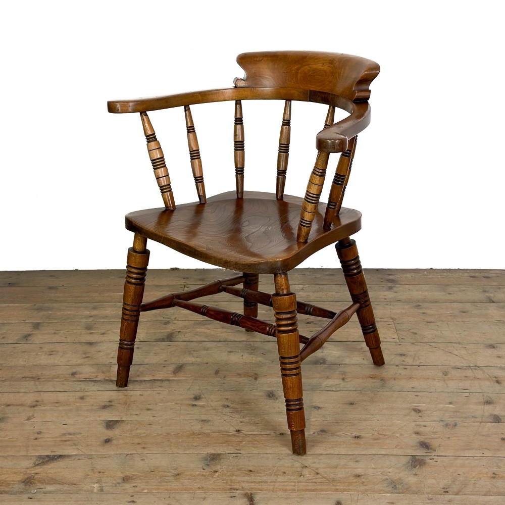 A warm brown wooden smokers bow armchair featuring turned legs, vertical back spindles, a steam-bent curved top rail, and a shaped solid seat.