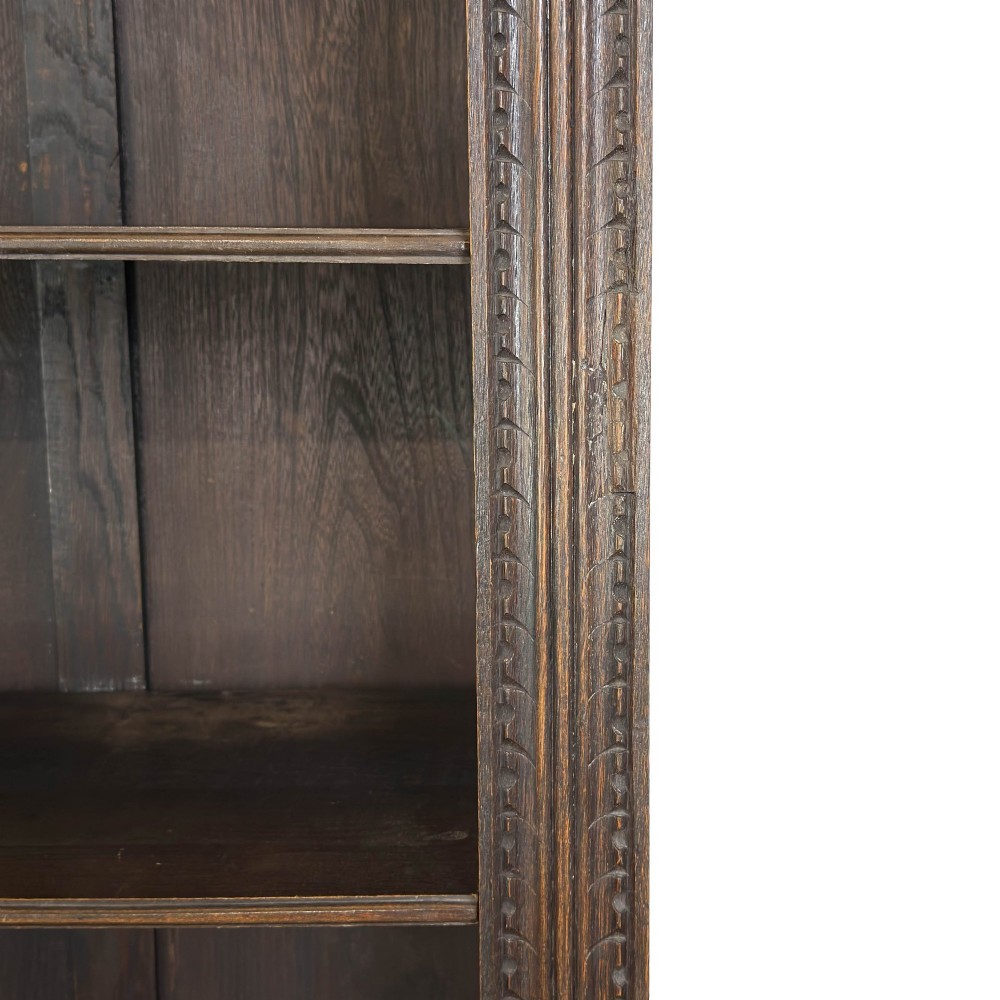 A tall dark oak open bookcase with multiple shelves, featuring carved floral scrollwork along the top frieze and fluted side columns. View IV