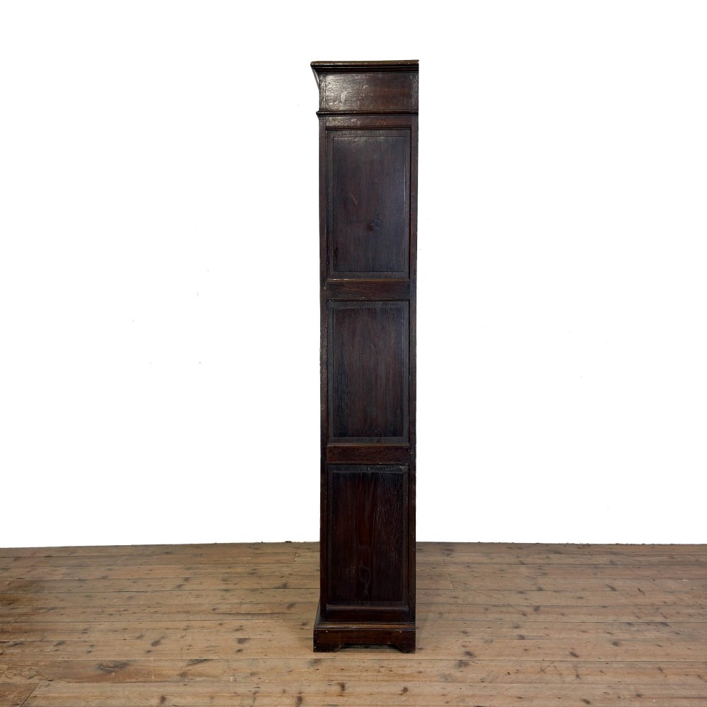 A tall dark oak open bookcase with multiple shelves, featuring carved floral scrollwork along the top frieze and fluted side columns. View V