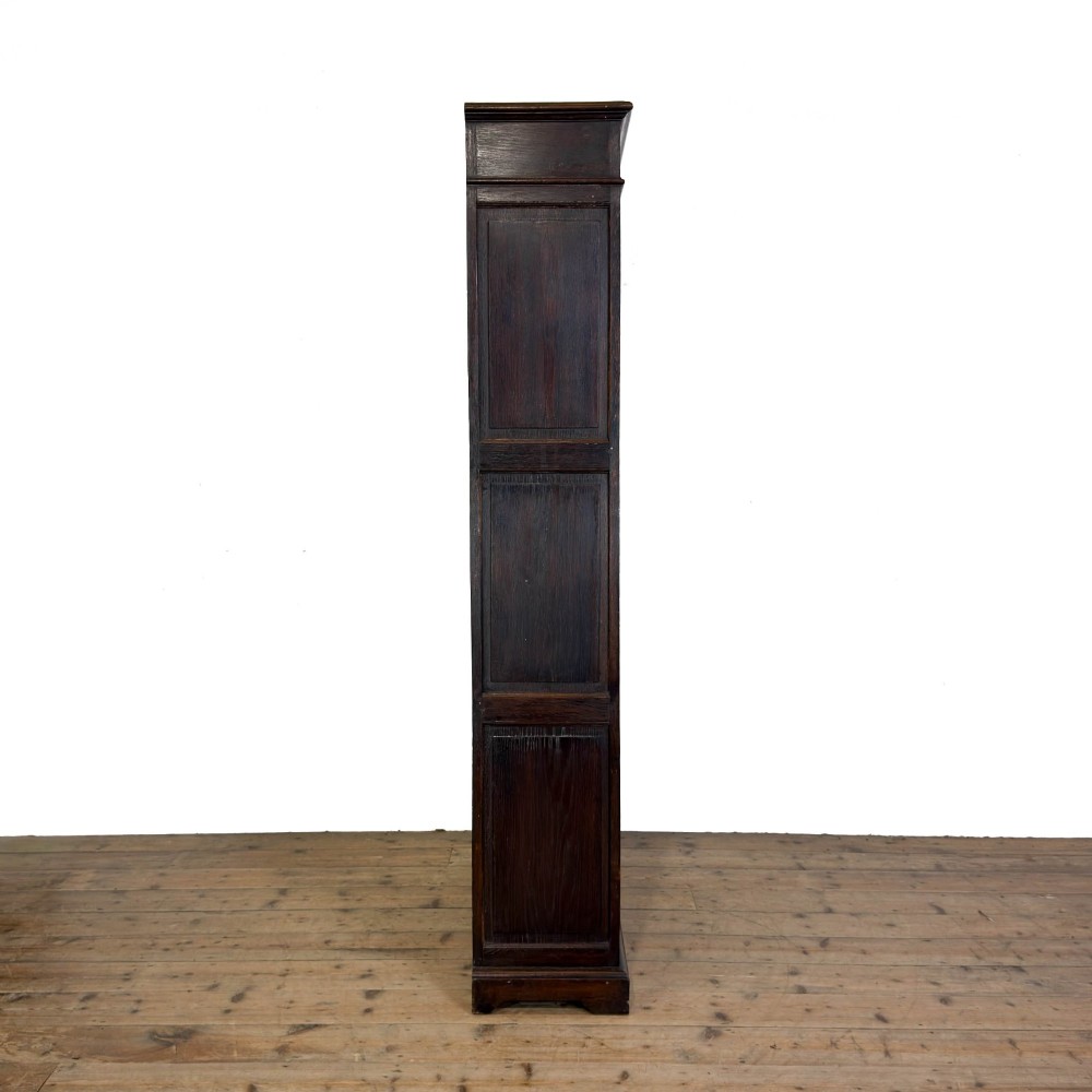 A tall dark oak open bookcase with multiple shelves, featuring carved floral scrollwork along the top frieze and fluted side columns. View VII