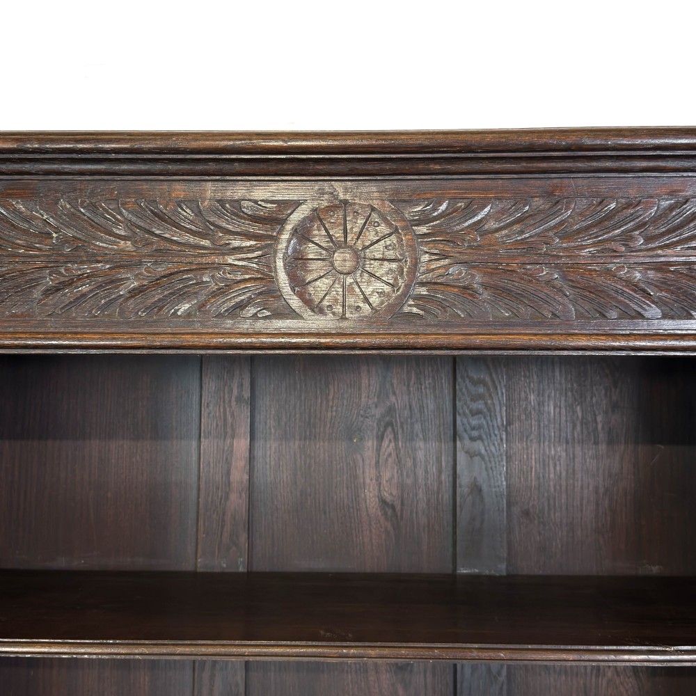A tall dark oak open bookcase with multiple shelves, featuring carved floral scrollwork along the top frieze and fluted side columns. View VIII