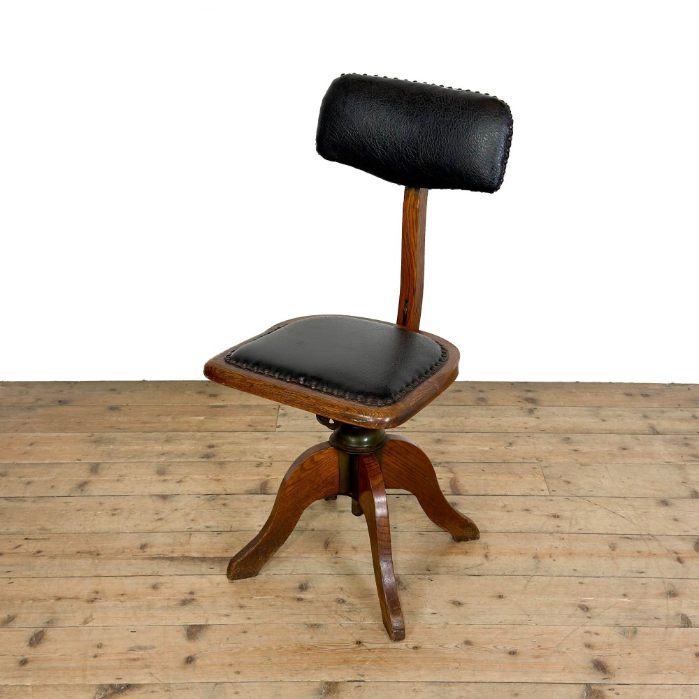 An early 20th-century oak swivel desk chair featuring dark studded leather upholstery, a curved lumbar backrest, and a four-star wooden base.