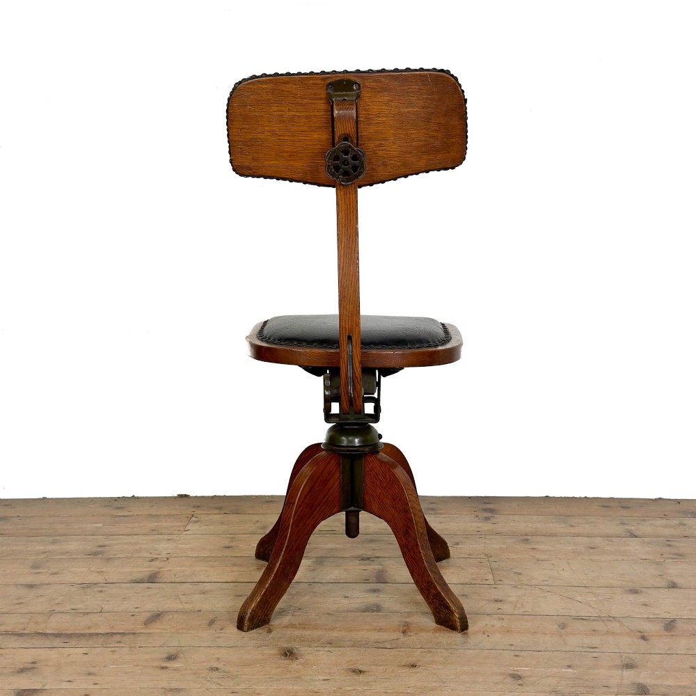 An early 20th-century oak swivel desk chair featuring dark studded leather upholstery, a curved lumbar backrest, and a four-star wooden base. View III