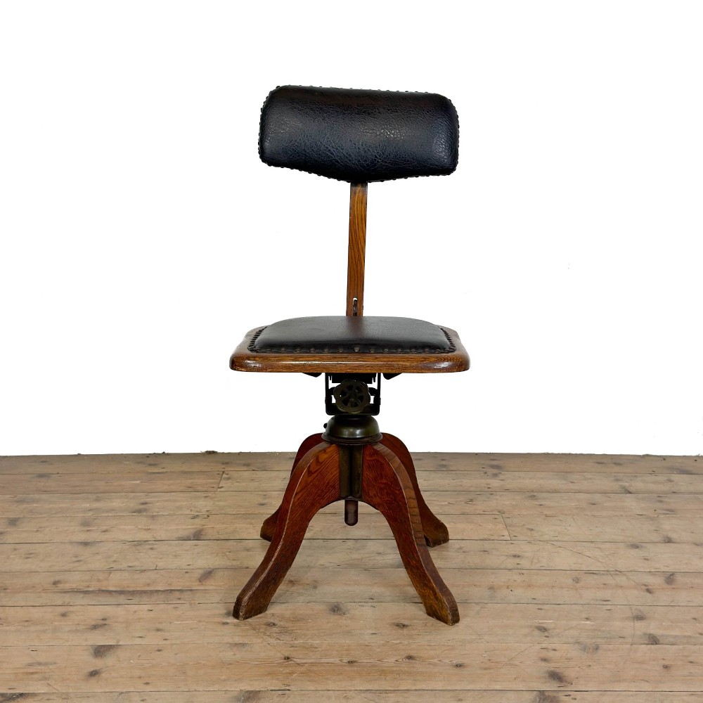 An early 20th-century oak swivel desk chair featuring dark studded leather upholstery, a curved lumbar backrest, and a four-star wooden base. View IV