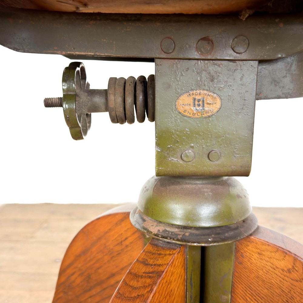 An early 20th-century oak swivel desk chair featuring dark studded leather upholstery, a curved lumbar backrest, and a four-star wooden base. View VII