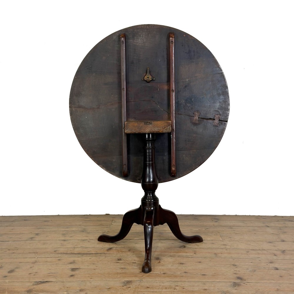 An antique George III mahogany tripod table featuring a circular tilt top shown in the upright position above a turned column and three down-swept legs. View IX