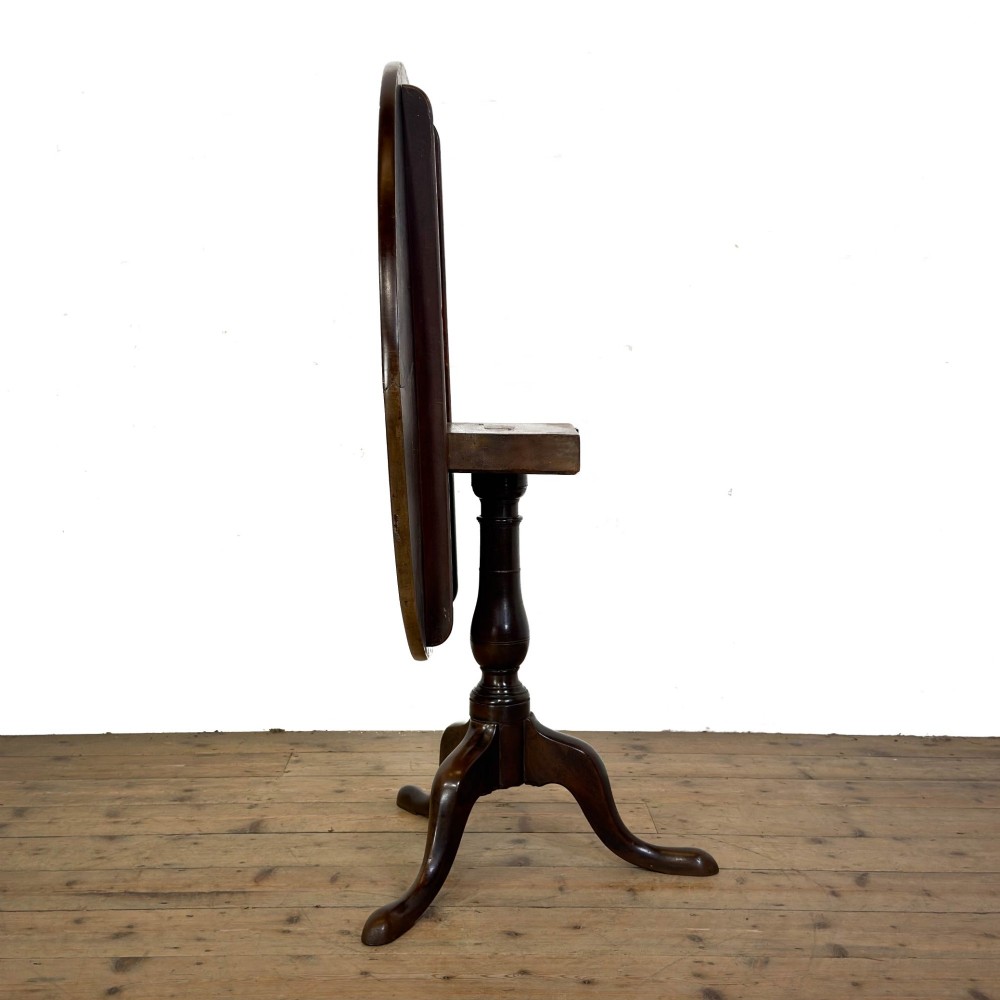 An antique George III mahogany tripod table featuring a circular tilt top shown in the upright position above a turned column and three down-swept legs. View XIII