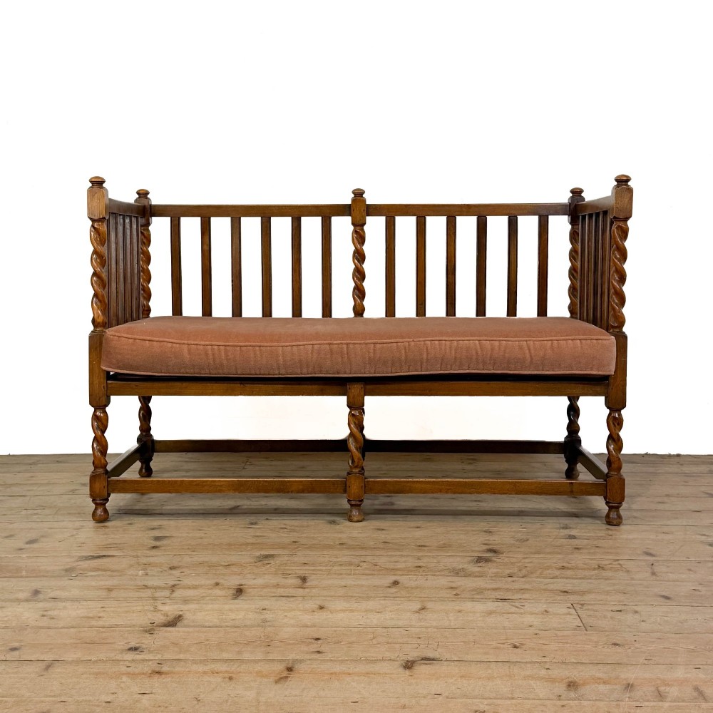An Arts and Crafts style oak hall bench featuring barley twist legs and side posts, a vertical slat backrest, and a terracotta-coloured cushion.
