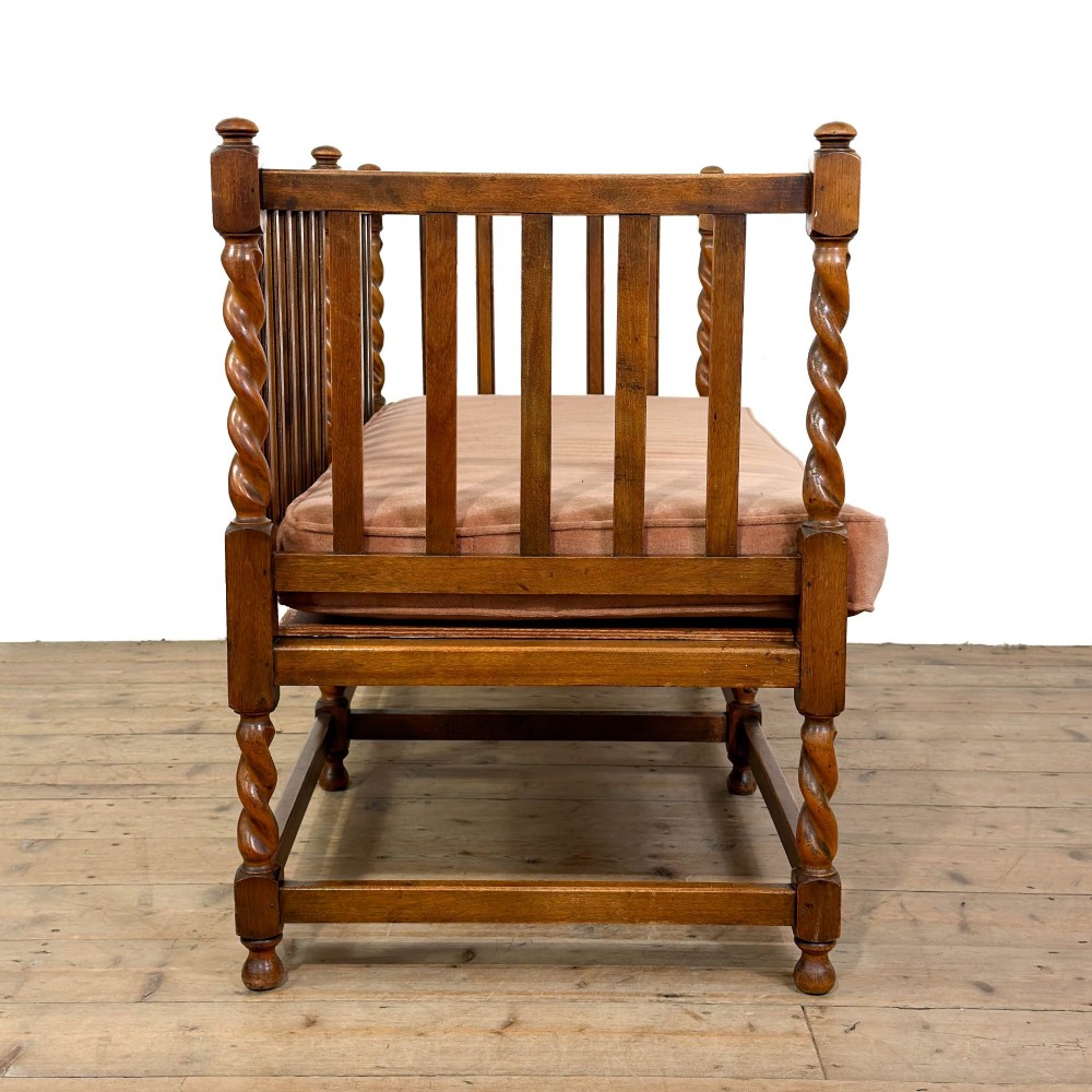 An Arts and Crafts style oak hall bench featuring barley twist legs and side posts, a vertical slat backrest, and a terracotta-coloured cushion. View VII