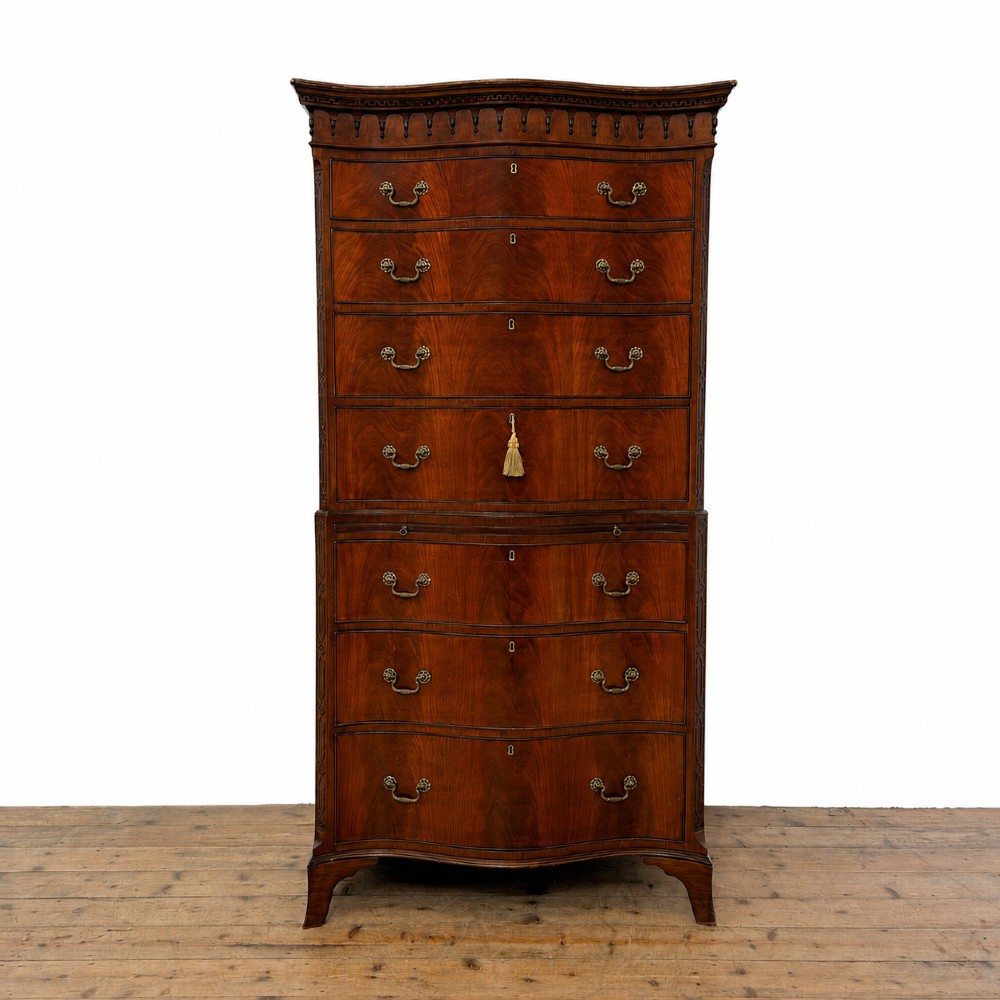 A tall mahogany serpentine chest on chest featuring two stacked sections of graduating drawers with brass handles and carved cornice detail.