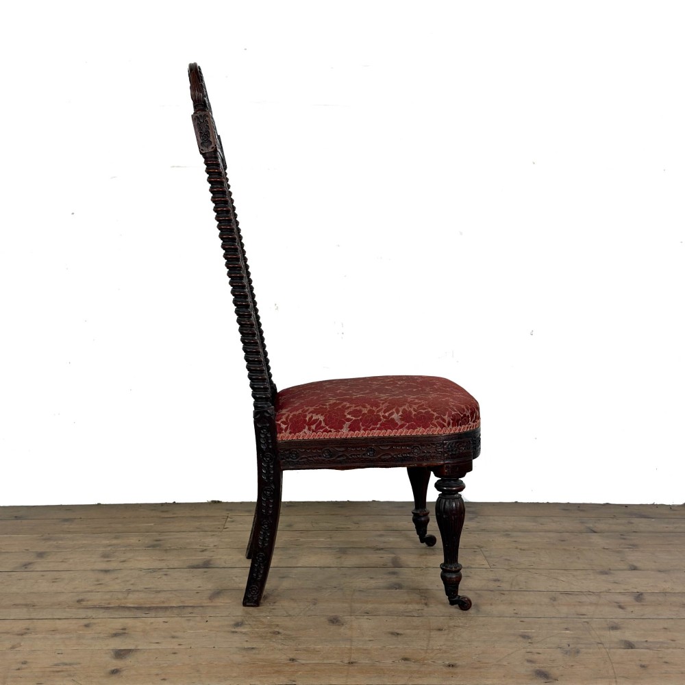A 19th-century Anglo-Indian chair with an intricately hand-carved lattice backrest, dark wood frame, turned legs on castors, and a patterned red upholstered seat. View II