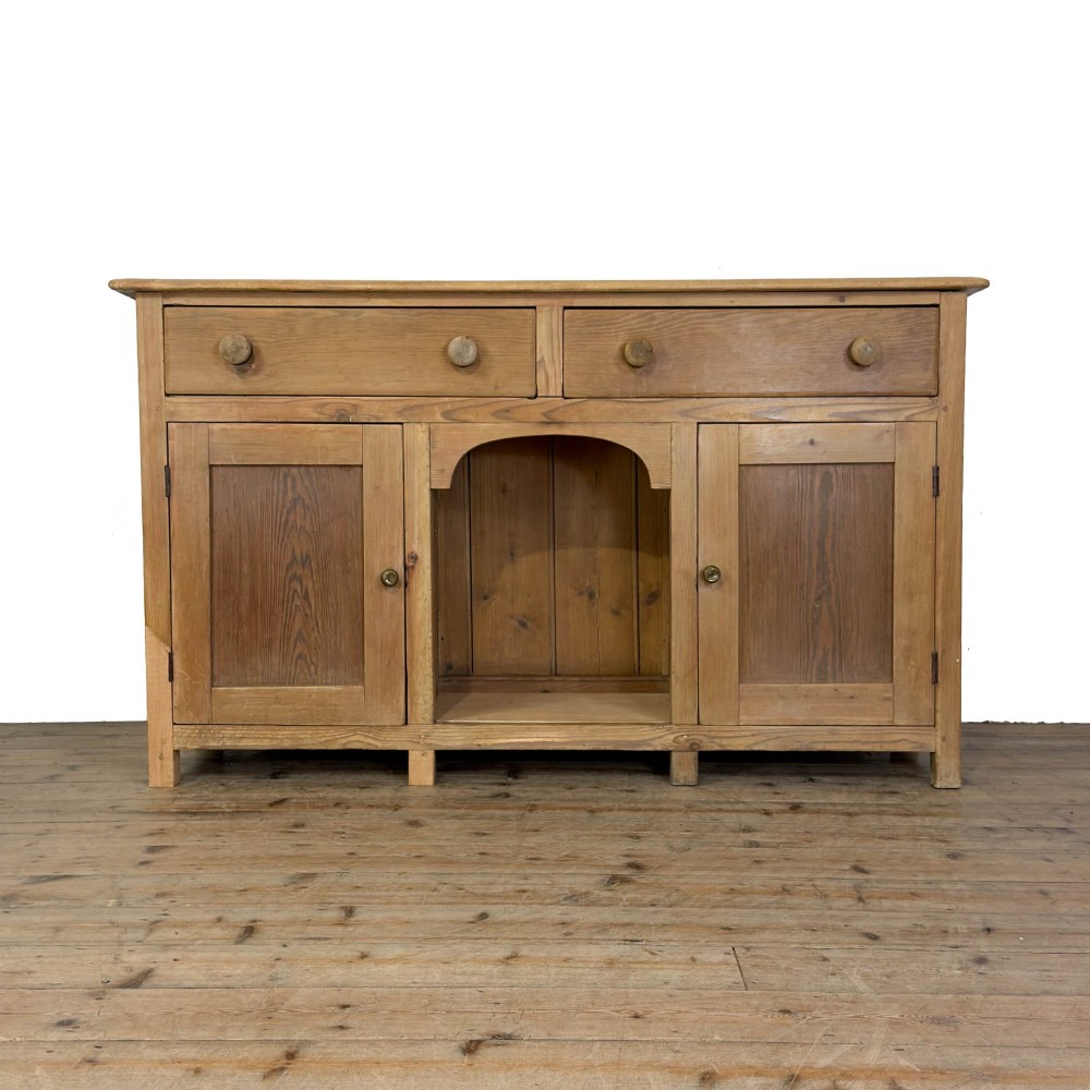 A Victorian pine dresser base featuring two top drawers with turned wooden knobs above two panelled cupboard doors and a central open arched niche.