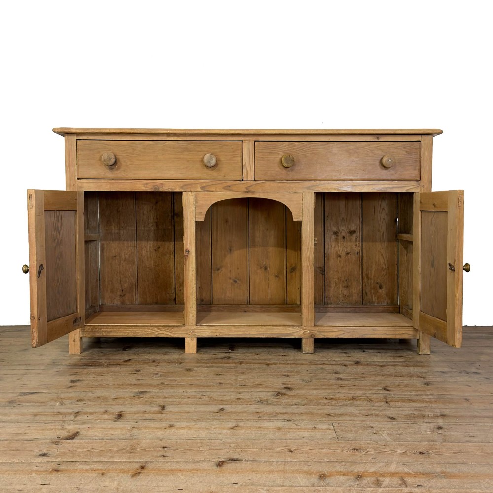 A Victorian pine dresser base featuring two top drawers with turned wooden knobs above two panelled cupboard doors and a central open arched niche. View II