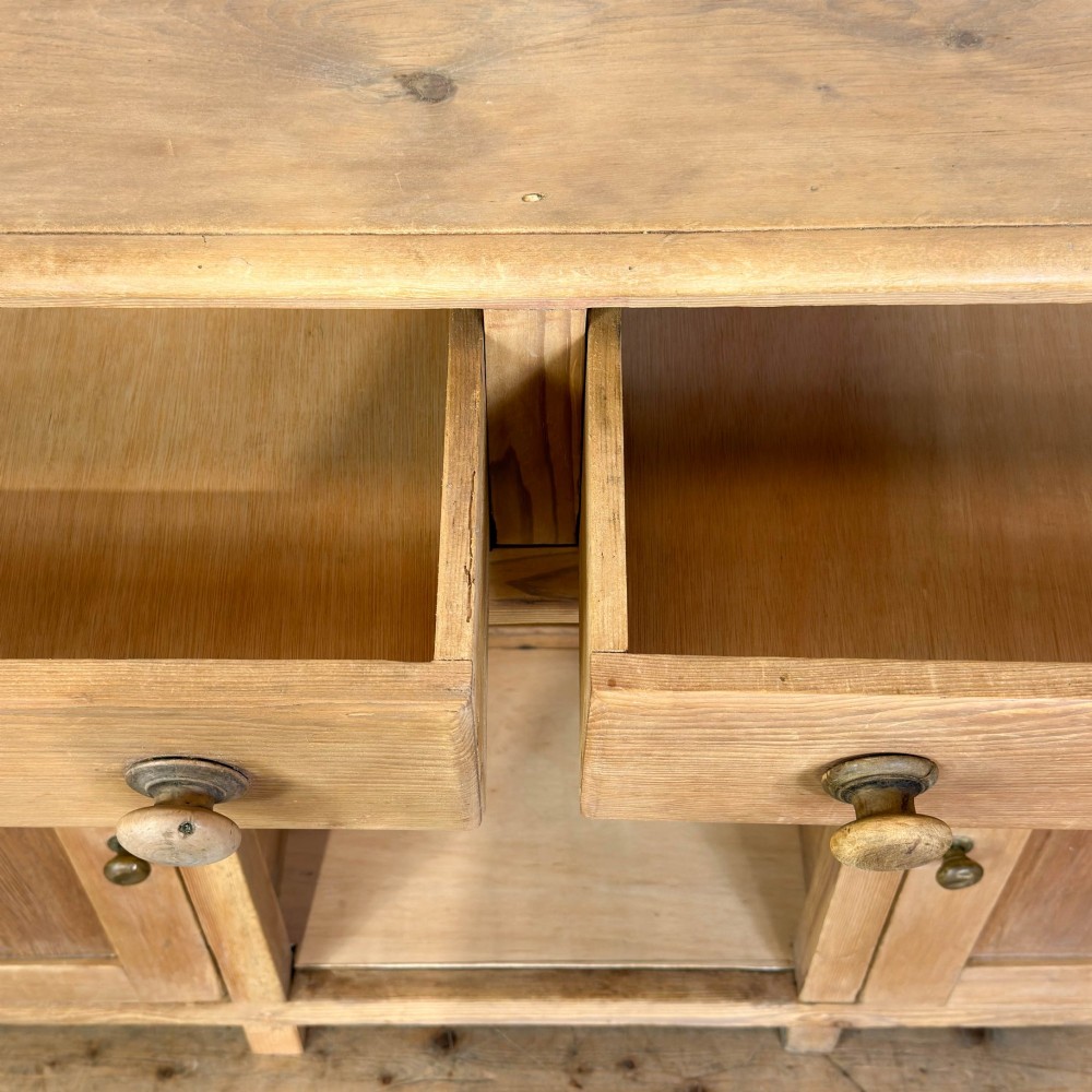 A Victorian pine dresser base featuring two top drawers with turned wooden knobs above two panelled cupboard doors and a central open arched niche. View III