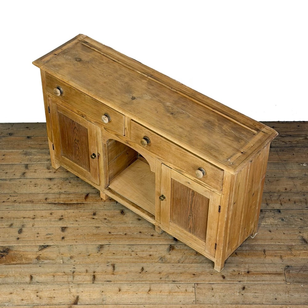 A Victorian pine dresser base featuring two top drawers with turned wooden knobs above two panelled cupboard doors and a central open arched niche. View V