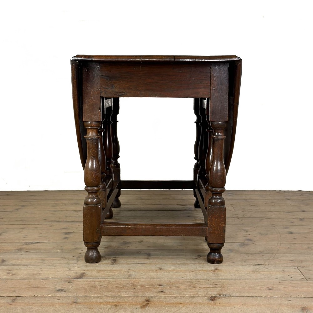 An 18th-century dark oak gateleg table featuring two hinged drop leaves, turned legs, and lower stretchers. View III