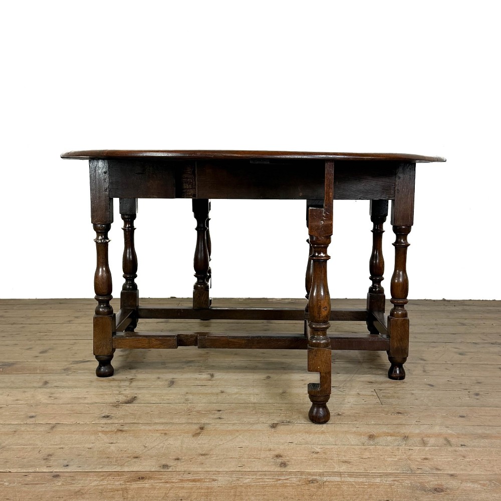 An 18th-century dark oak gateleg table featuring two hinged drop leaves, turned legs, and lower stretchers. View V