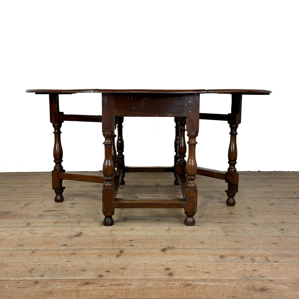 An 18th-century dark oak gateleg table featuring two hinged drop leaves, turned legs, and lower stretchers. View VIII